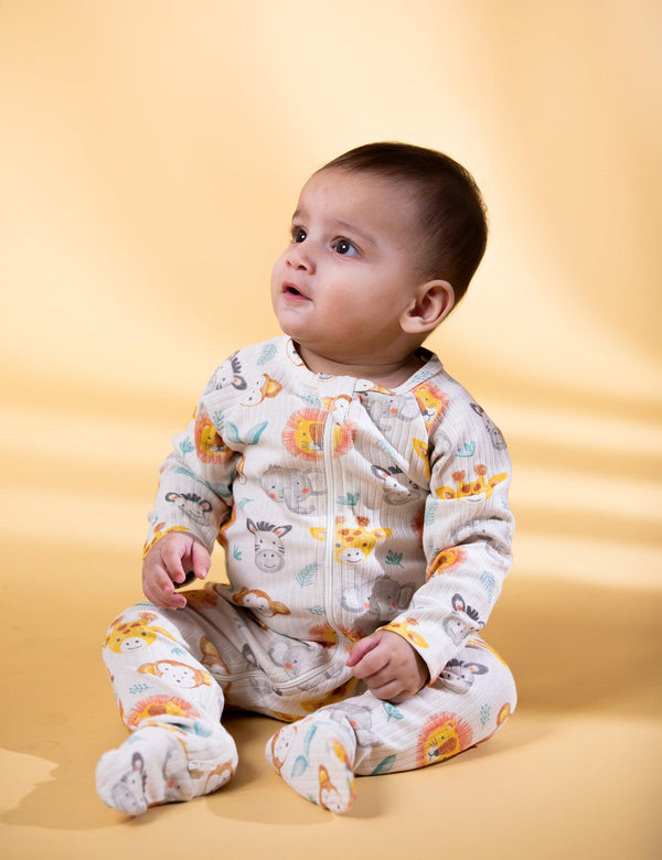 A cute baby, who appears to be of mixed ethnicity, sitting and looking up while wearing a organic cotton footie with a colorful safari animal print. Shop soft baby Growsuit India.