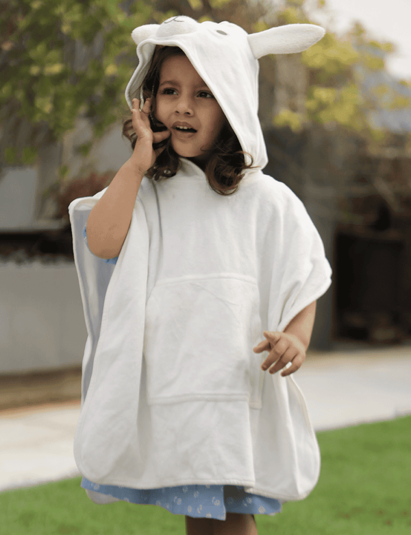 A young child, who appears to be of South Asian descent, wearing a soft off-white organic cotton hooded towel designed like a bear with ears. Shop gentle baby towels India.