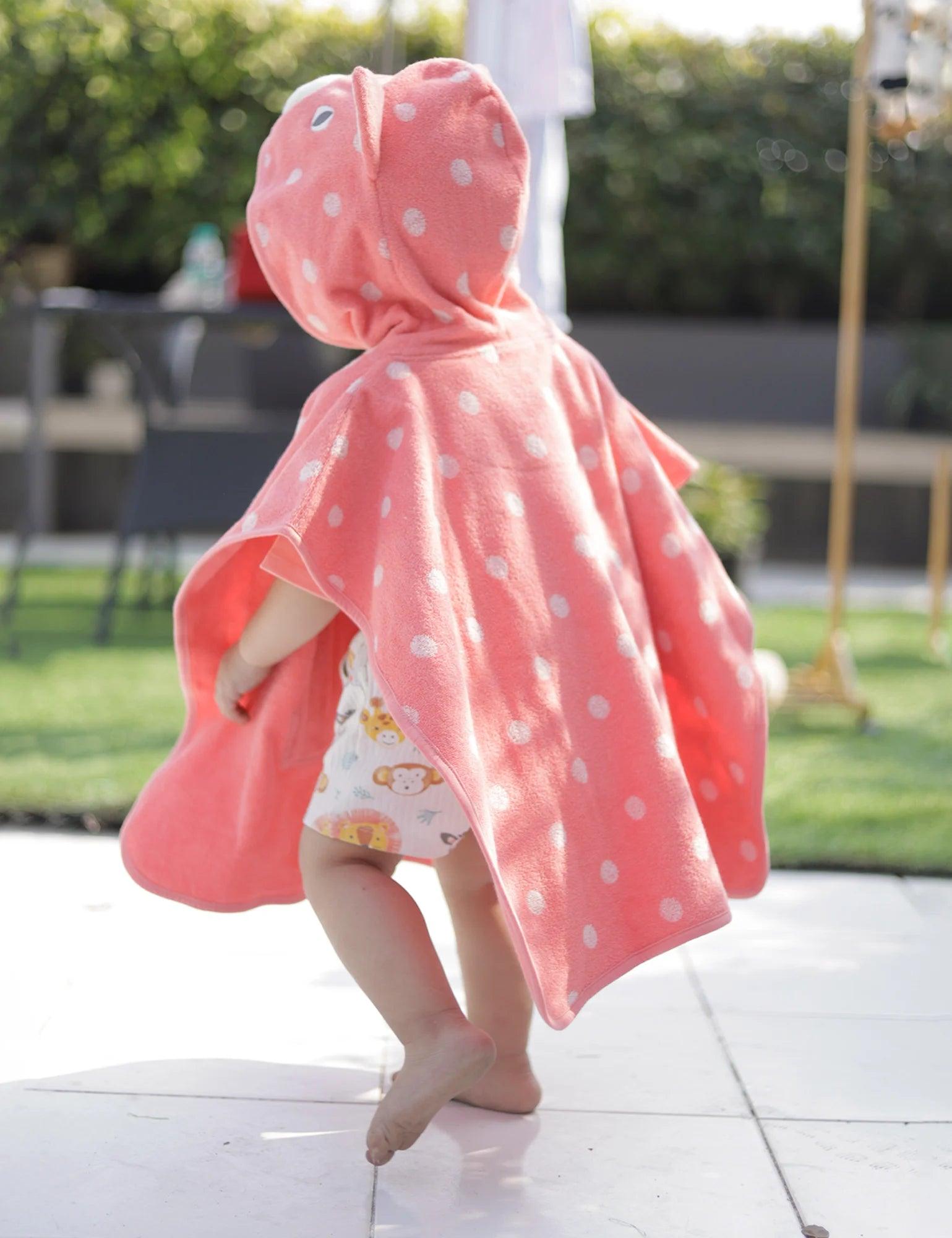 Baby wearing pink polka dot hooded towel with cat ears outdoors on tiled patio