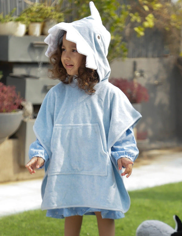 A young child, who appears to be of Caucasian descent, wearing a light blue organic cotton hooded towel designed like a shark with teeth. Shop fun baby towels India.