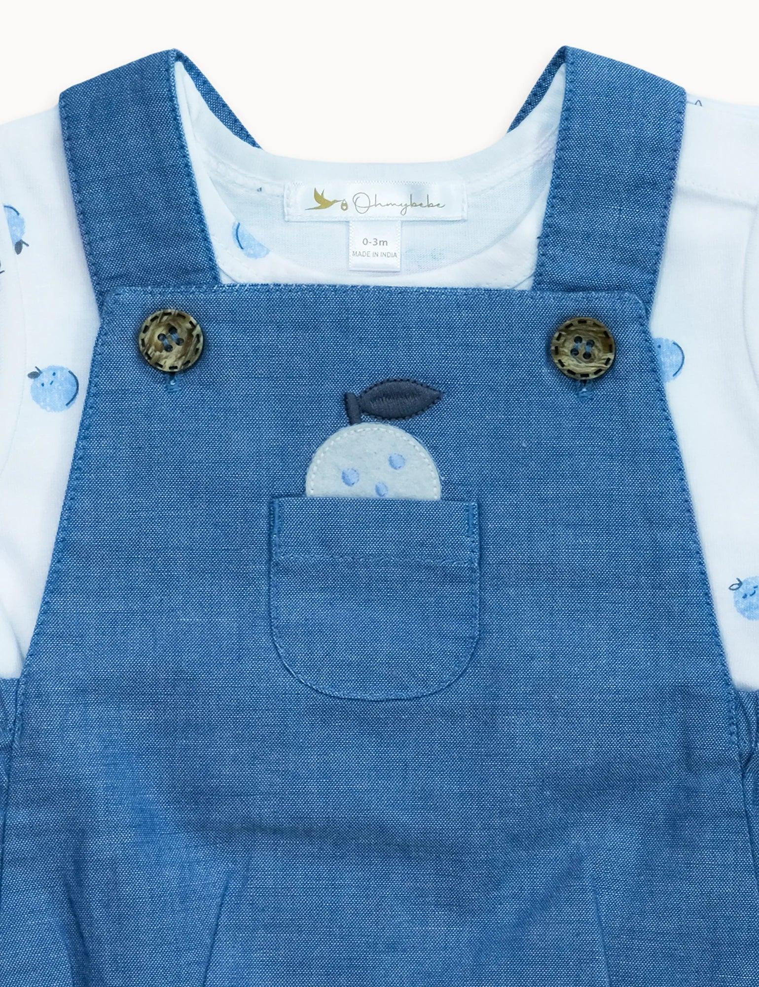 Blue organic cotton baby dungaree with apple pocket detail over white apple-print shirt