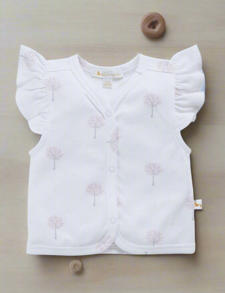 White organic cotton baby top with sweet flutter sleeves and a subtle print of winter trees. Features a v-neck and button-down front. Shop gentle baby tops India.