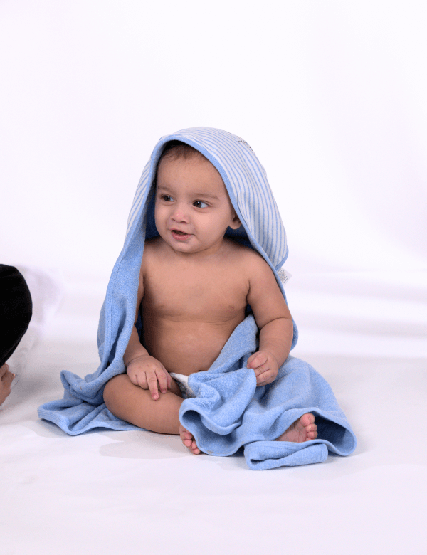 Baby wrapped in blue hooded towel sitting on white background, smiling and looking aside
