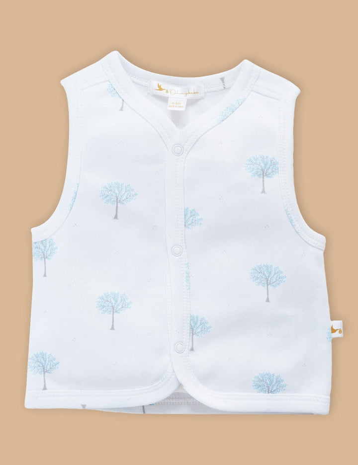 White organic cotton baby sleeveless top with a v-neck and button closure, featuring a subtle blue winter tree print. Shop gentle baby tops India.