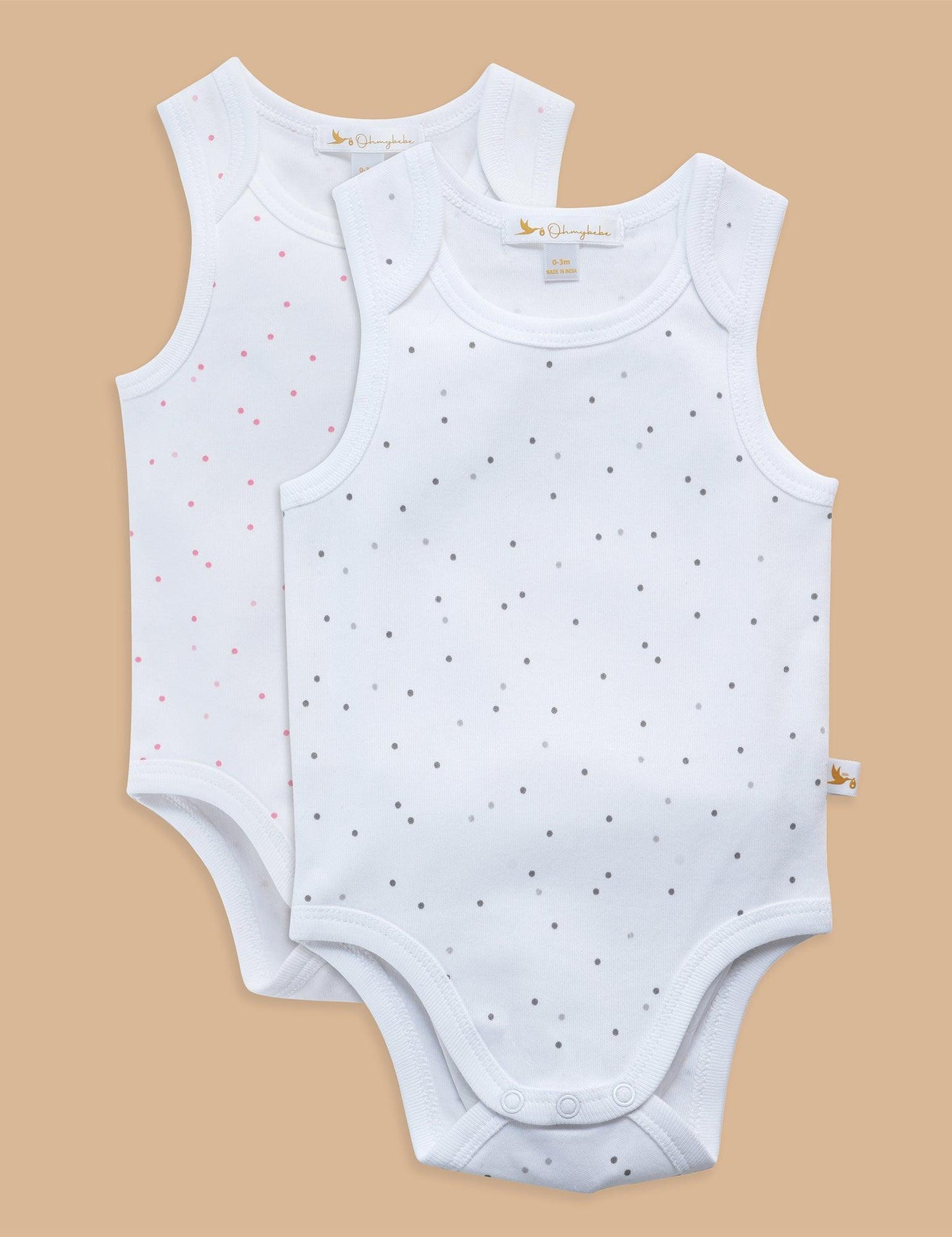 Two white sleeveless organic cotton baby bodysuits with gray and pink polka dots on beige background