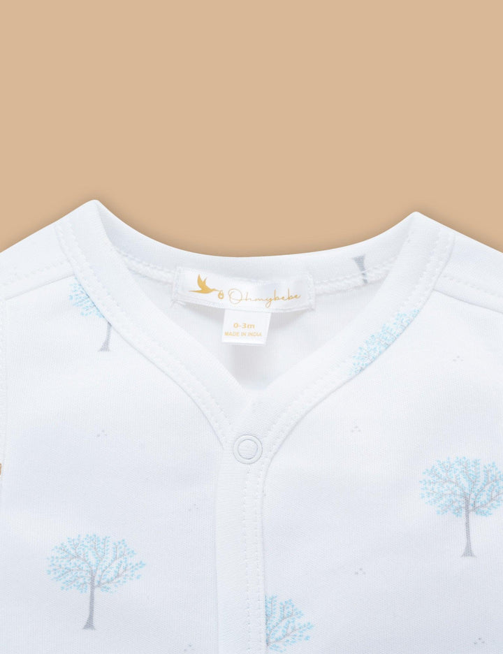 Close-up of the white organic cotton sleeveless baby top showing the v-neck and button detail, with the blue winter tree print. See organic baby wear India.