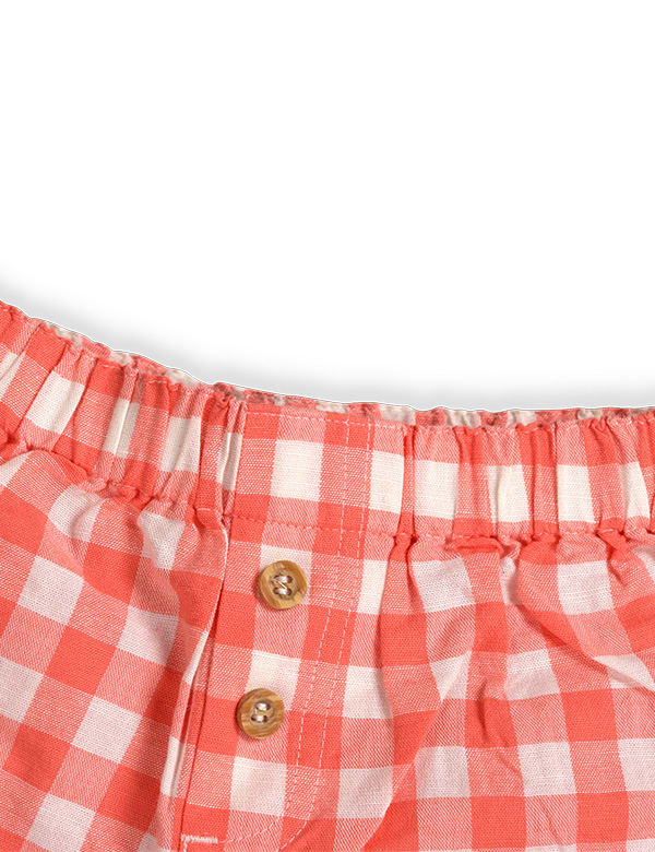Close-up of wooden button placket and elastic waistband on peach gingham baby shorts