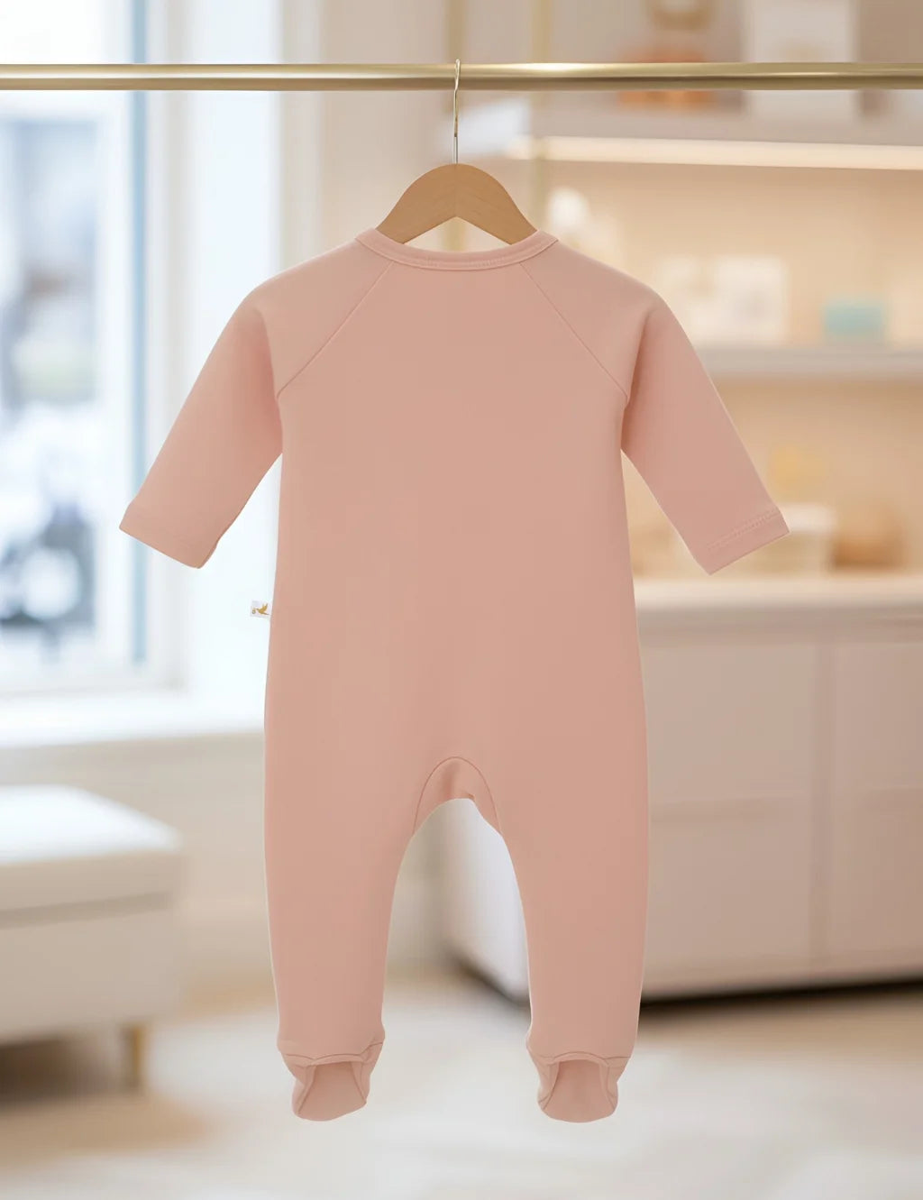Pink baby onesie on a hanger with a blurred indoor background