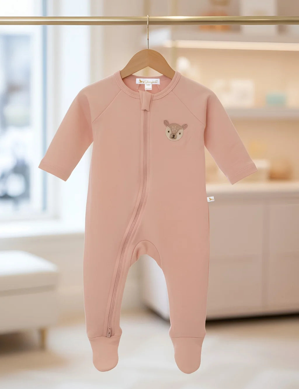 Pink baby onesie with a deer design on a hanger in a room.