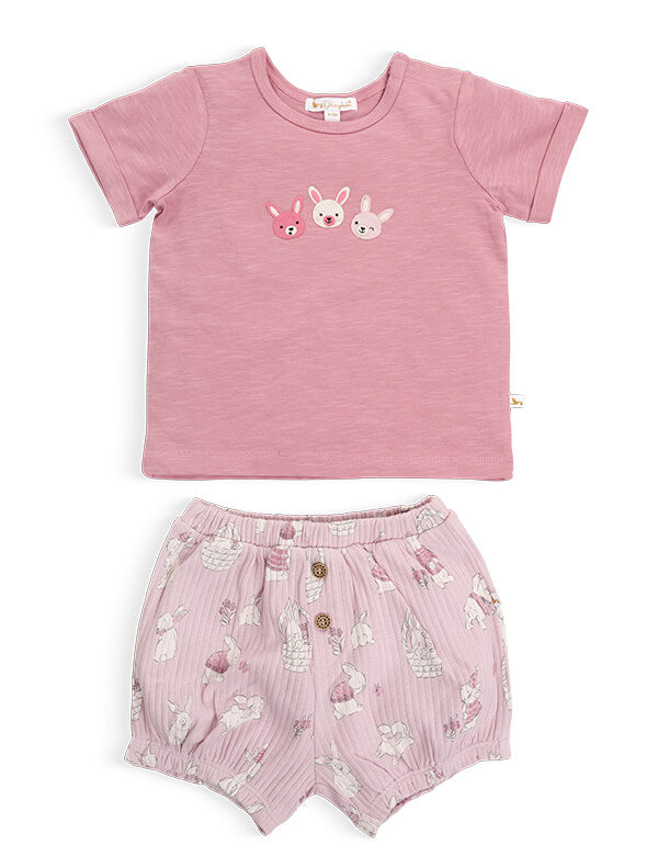 Flat lay of an organic cotton pink short-sleeve tee with three embroidered bunnies and patterned shorts.