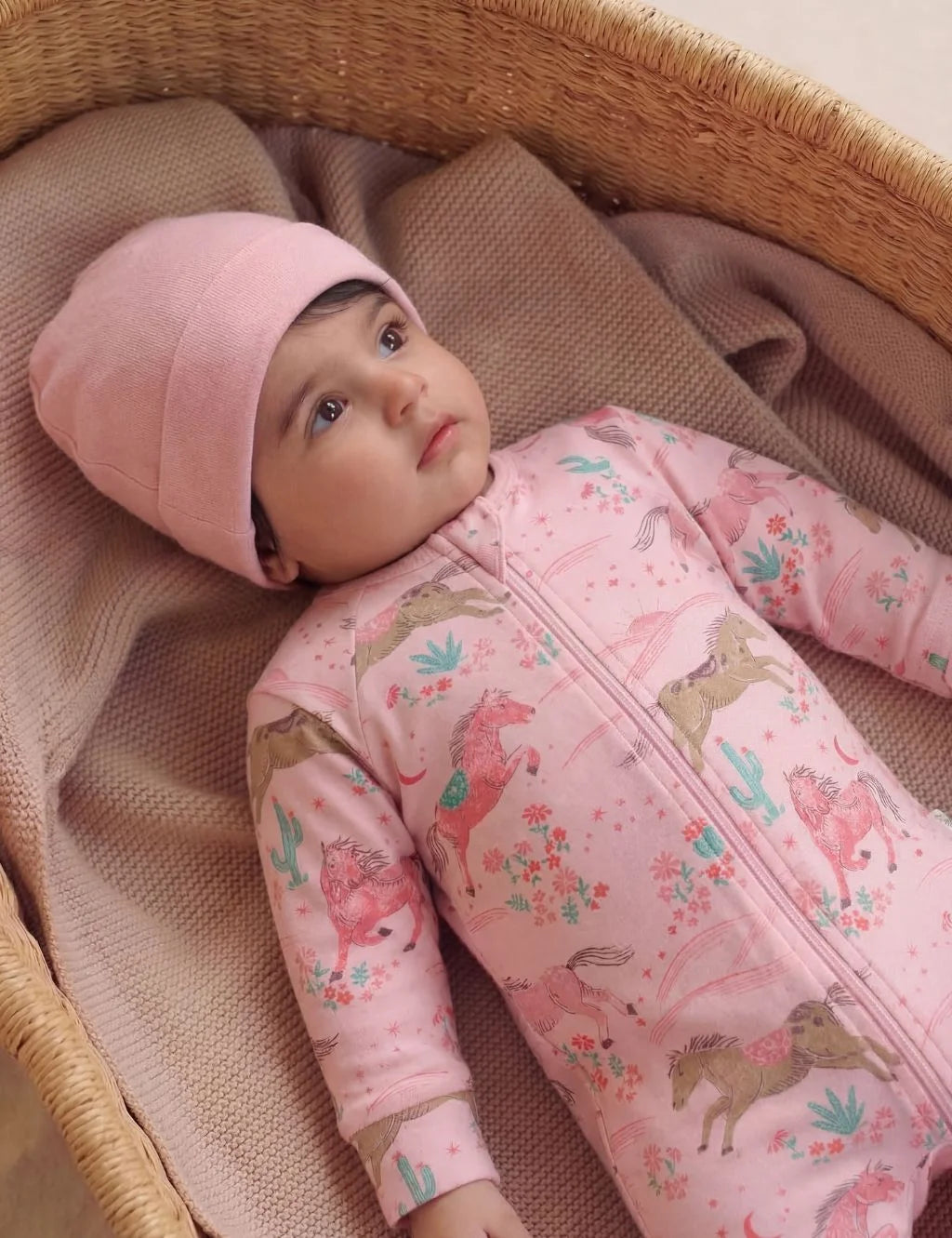 Newborn baby wearing a pink organic cotton zipper romper featuring a desert horse print.