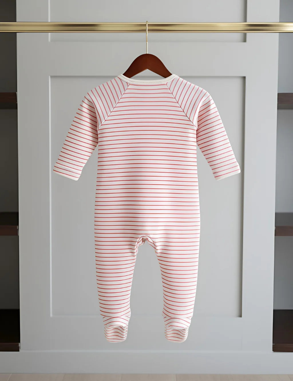 Pink and white striped baby onesie hanging on a wooden hanger against a white wall.