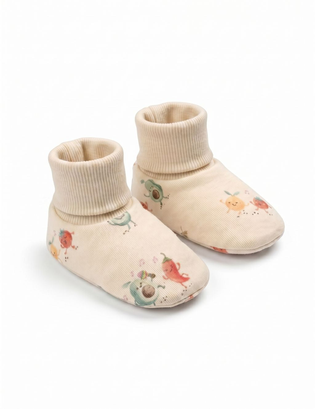 A pair of soft cream-colored baby booties featuring a playful print of smiling fruit and vegetable characters, including an avocado and a chili pepper, displayed against a plain white background.
