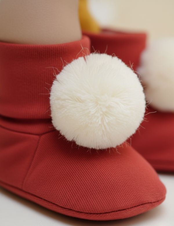 Red baby booties with white pom-poms on a neutral background
