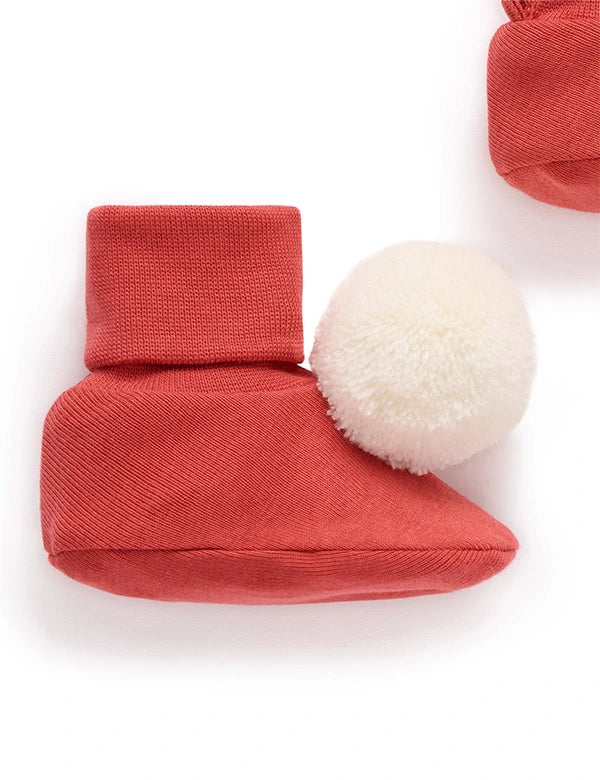 Red baby booties with a white pom-pom on a white background