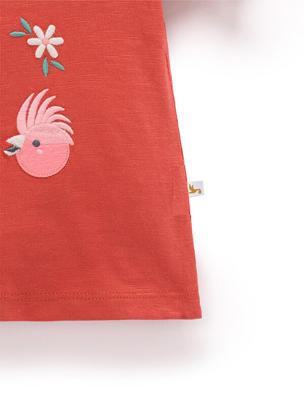 Red fabric with pink rooster design and white flower on a white background