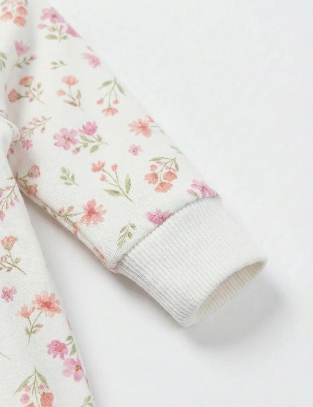 Close-up detail of the ribbed sleeve cuff on the white organic cotton baby growsuit featuring a delicate pink floral pattern.