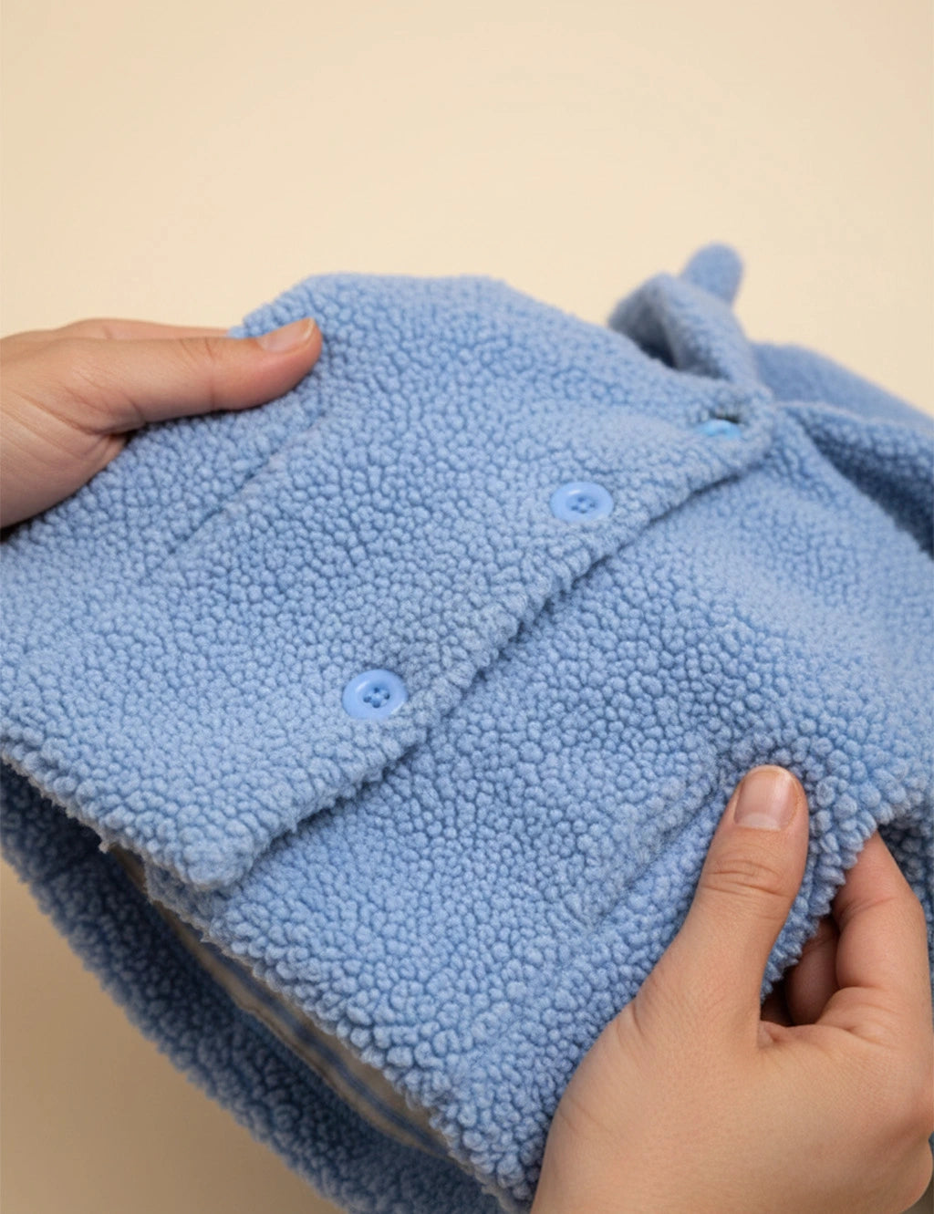 Blue textured fabric held by hands against a beige background