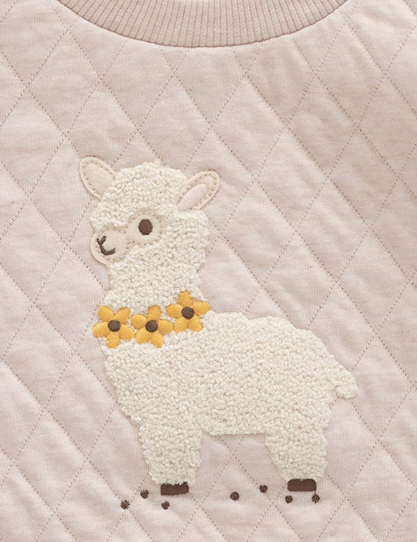 Close-up of beige quilted fabric sweatshirt featuring a textured white llama with yellow flower necklace embroidery