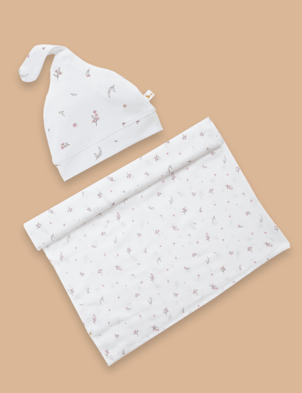 Vanilla Blossom baby wrap and cap set with delicate floral print on soft white fabric against beige background