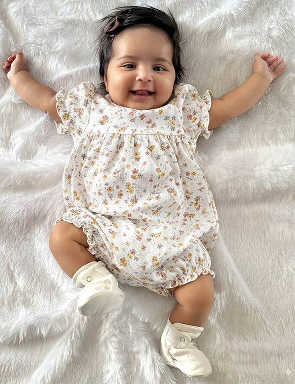 Smiling baby girl lying on white fuzzy blanket wearing floral dress and white booties