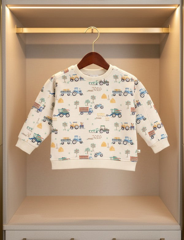 Children's cream sweatshirt with colorful tractor and farm print hanging on wooden hanger in wardrobe